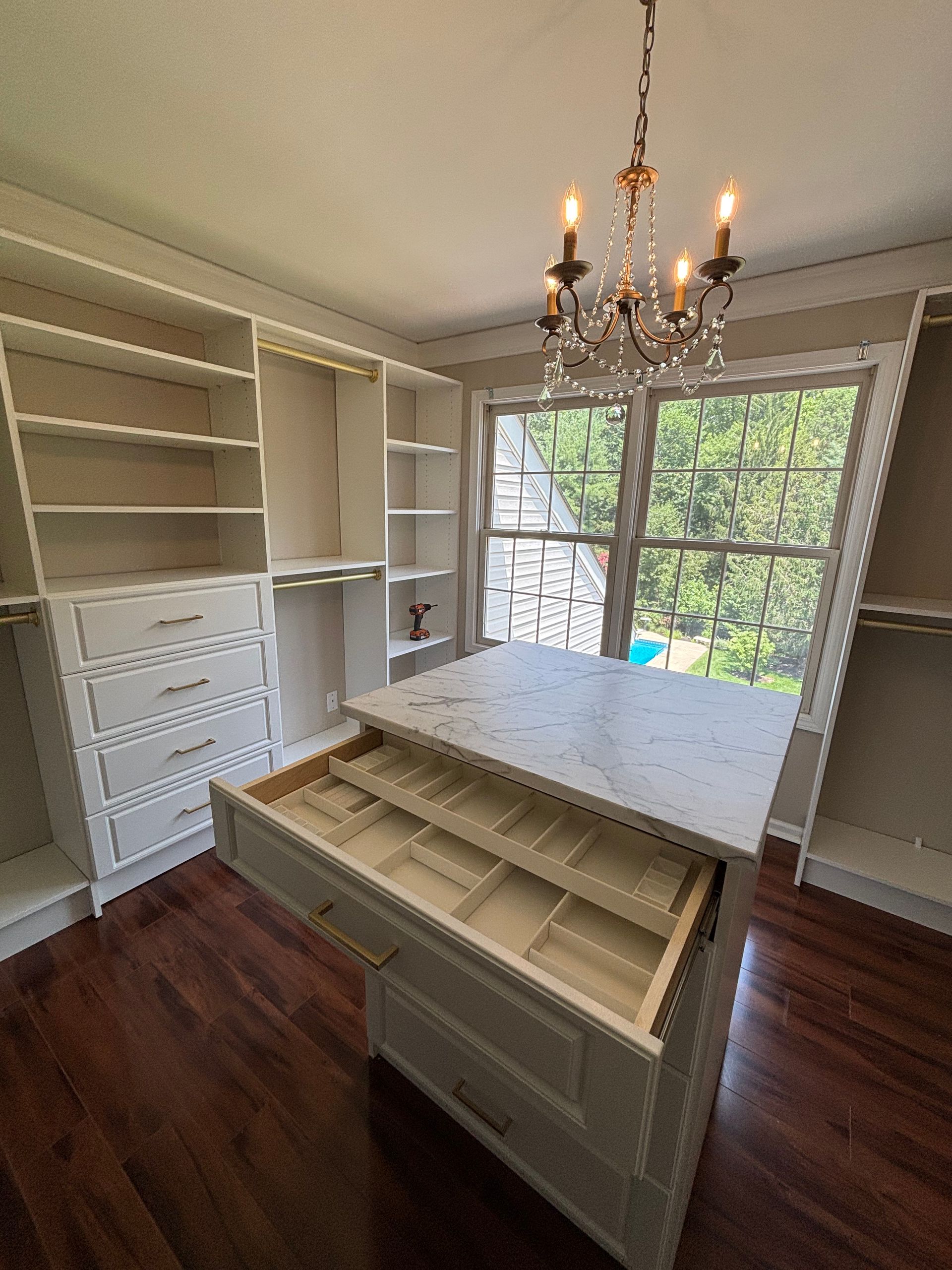 Bright empty room with built-in shelves, central island, chandelier, and large window view of trees