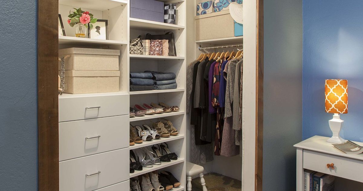 Walk-in closet with shelves and hanging clothes, white drawers, and brown trim. Blue walls and a bedside table are also visible.
