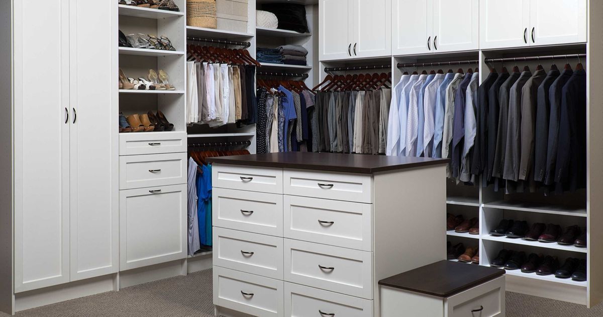 A walk-in closet featuring white cabinetry, hanging clothes, shelves with shoes, and a central island with drawers.