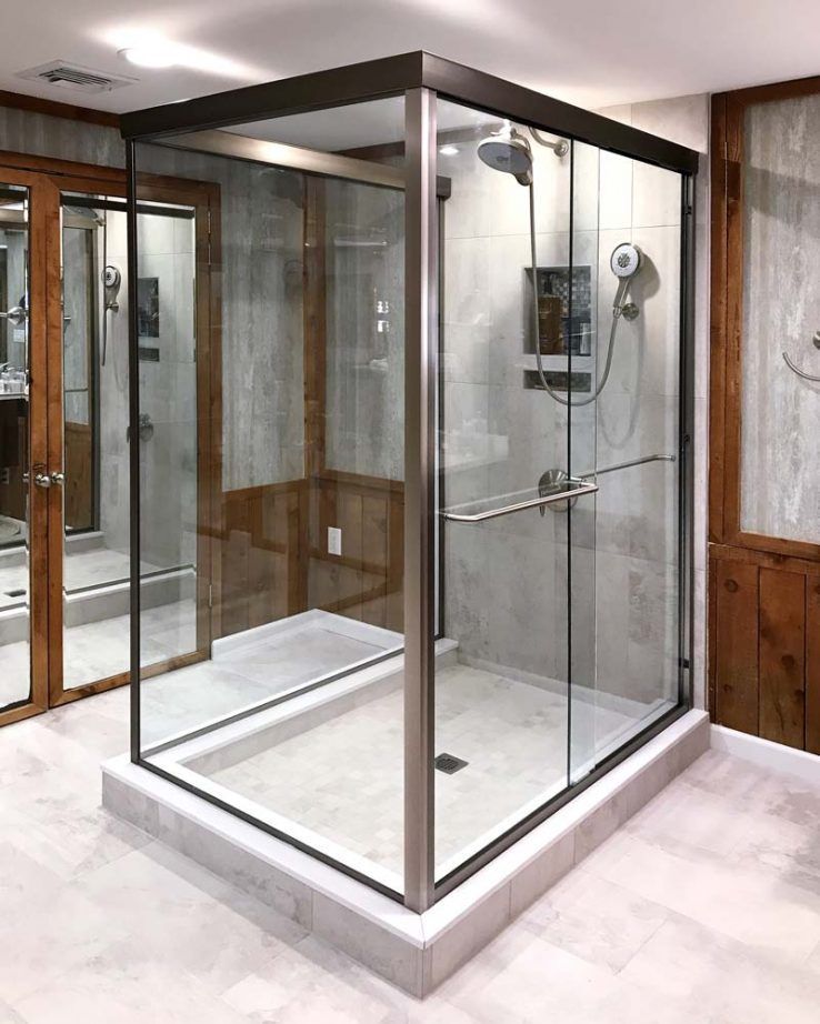 A modern, glass-enclosed shower stall with a dark metal frame, positioned in a bathroom with wood-paneled walls.