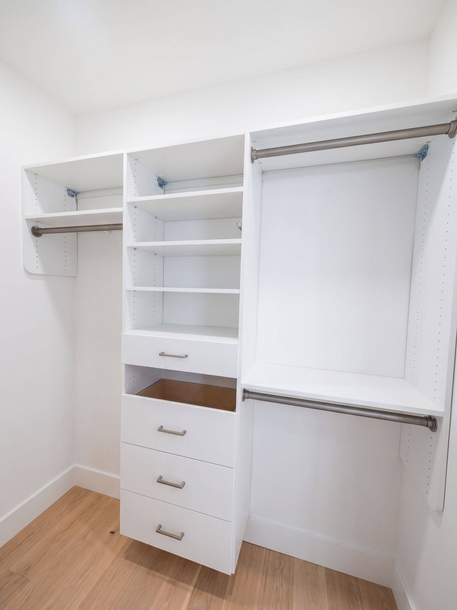 White built-in closet with open shelves, drawers, and hanging space in a bright empty room.