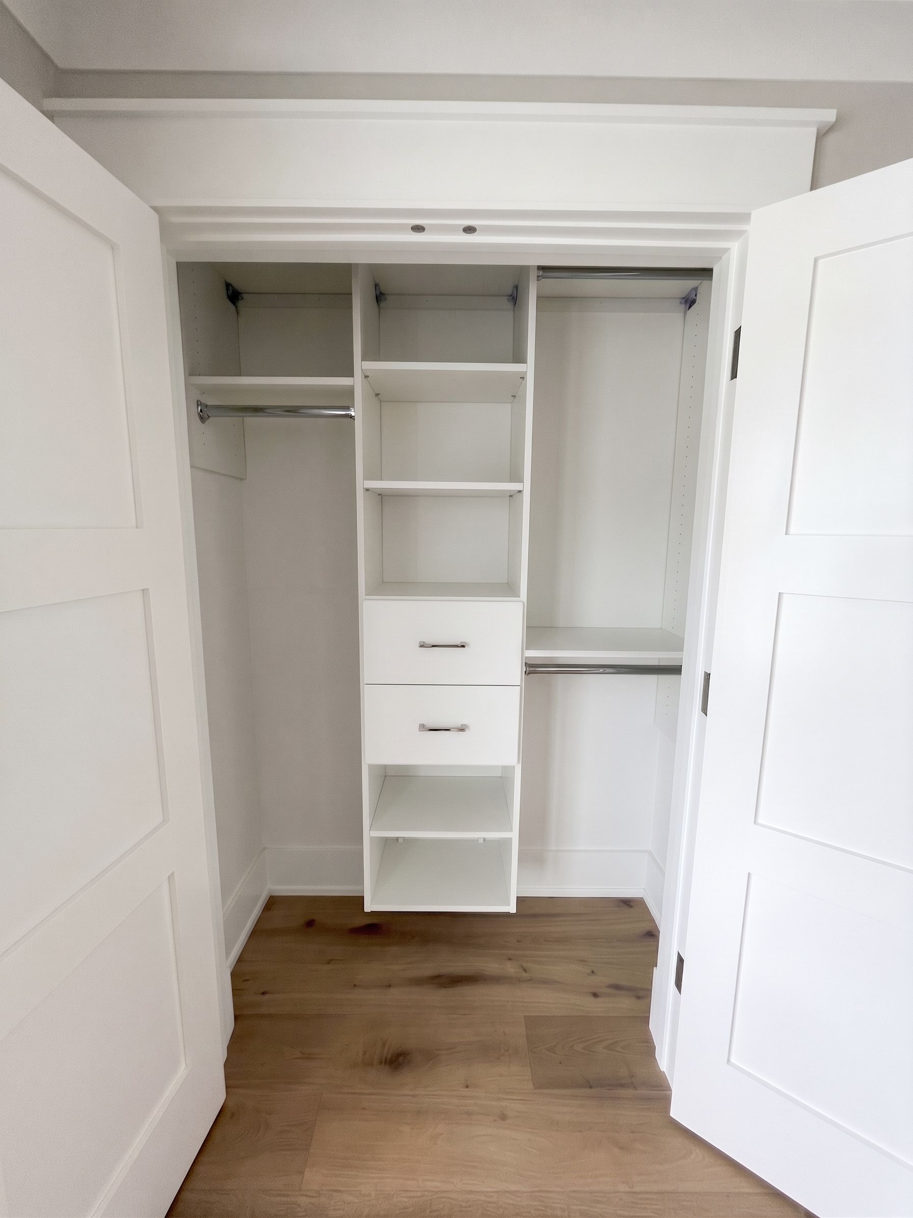 Open white closet with built-in shelves, drawers, and hanging space in a bright room