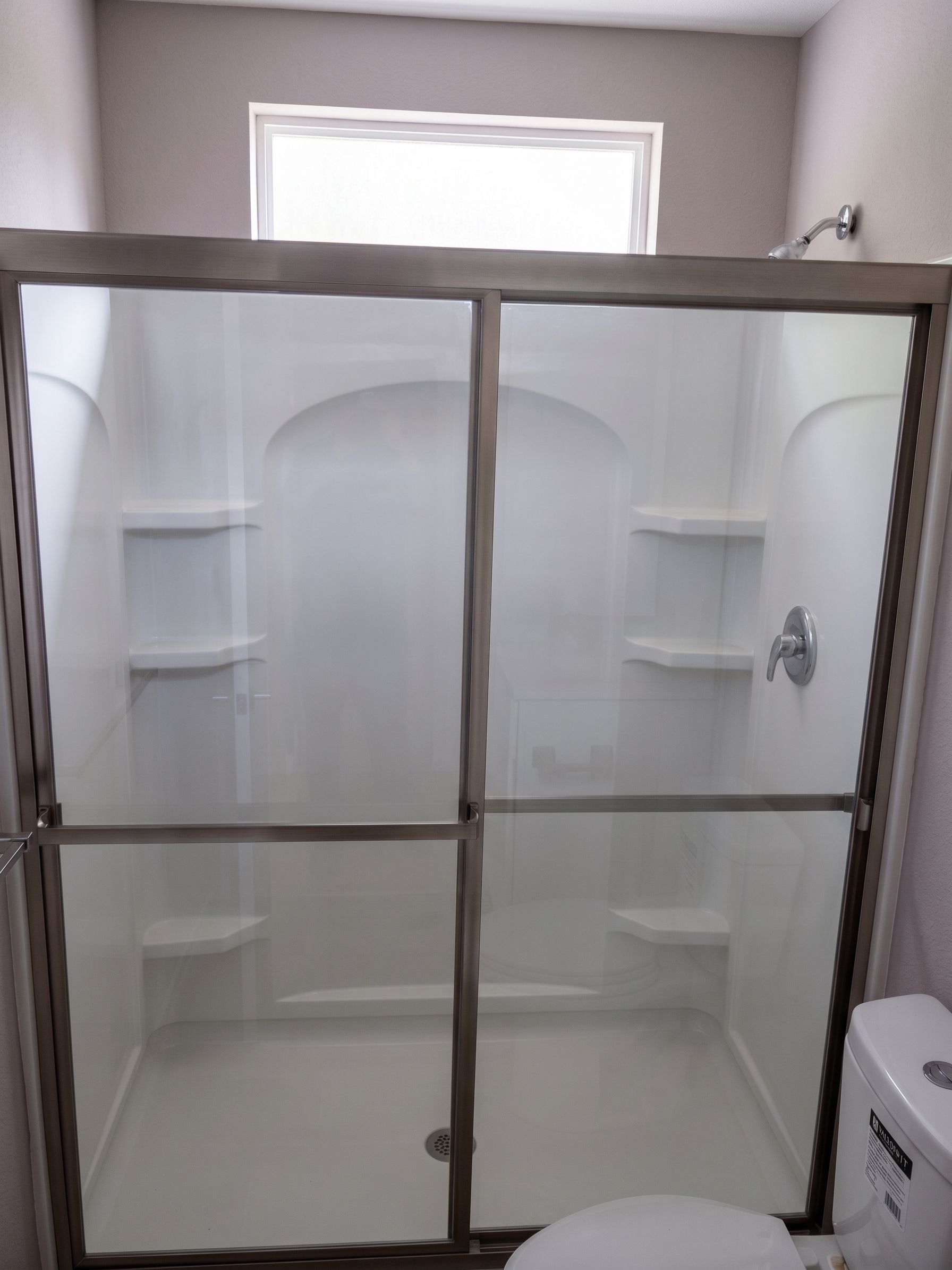 Glass shower enclosure with built-in corner shelves and a window above the tub.