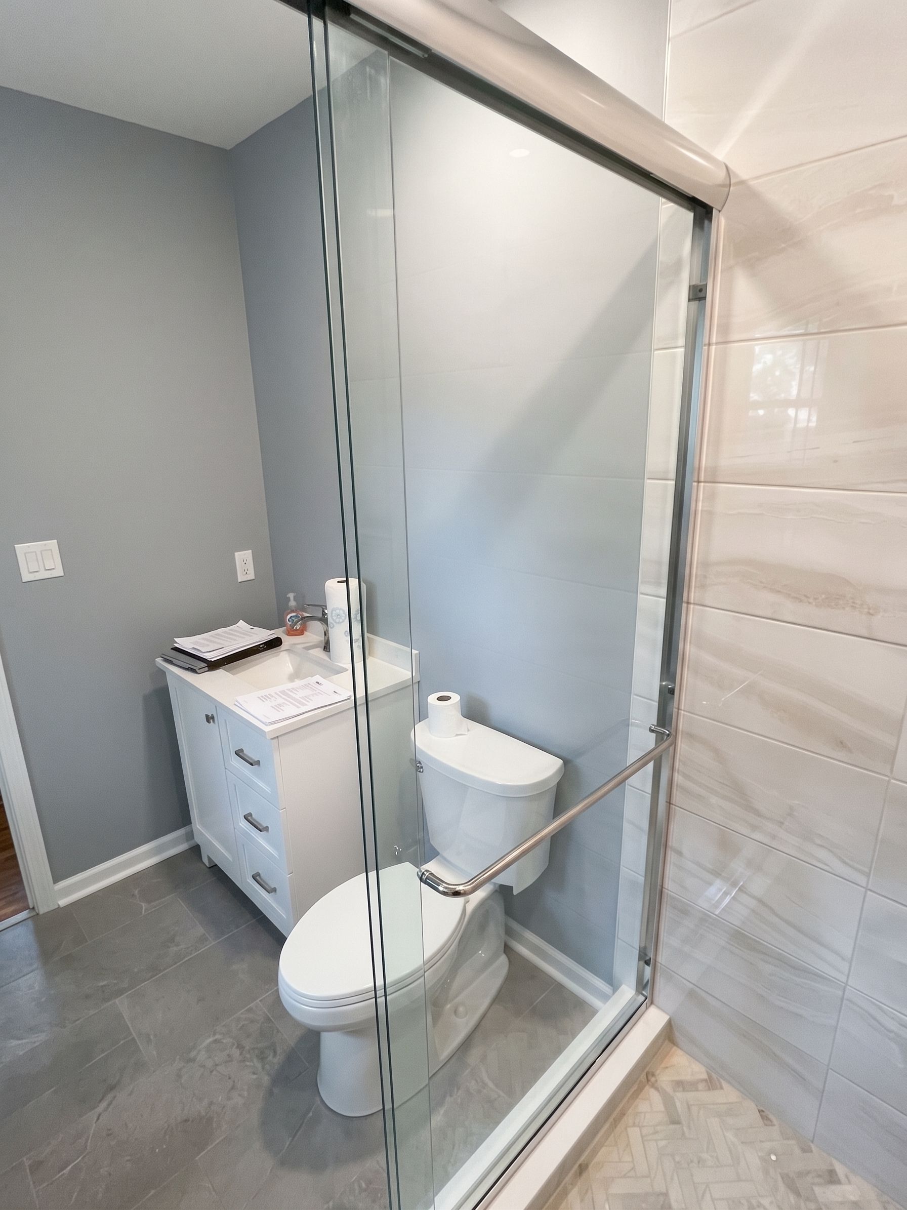 Bathroom with glass shower enclosure, white toilet, and small vanity beside a gray wall.