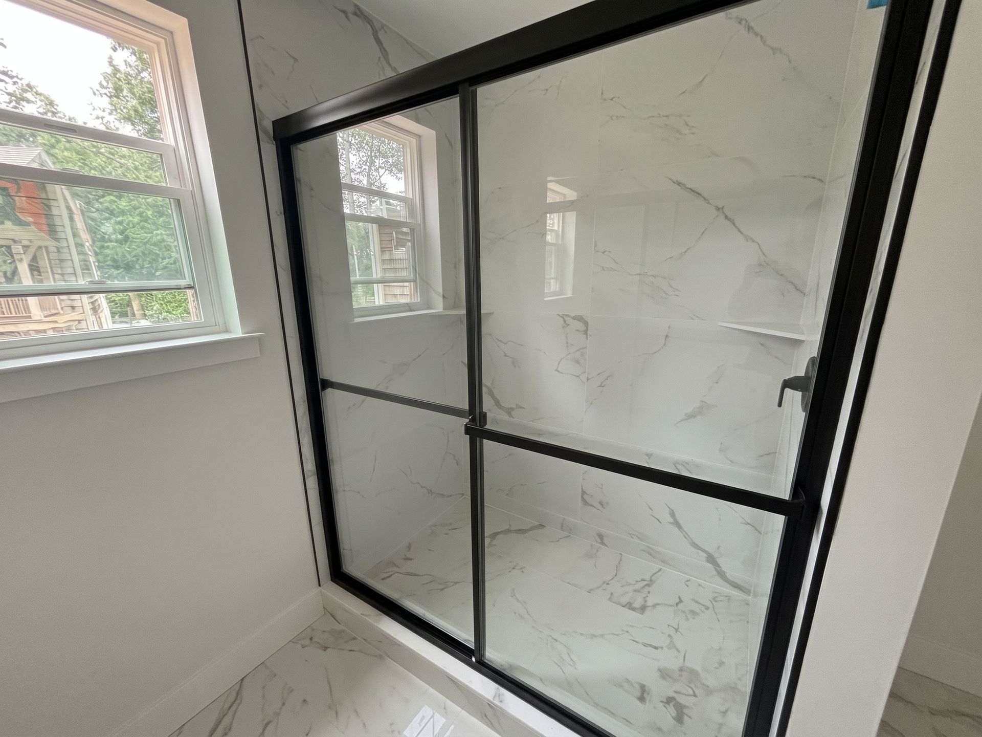 Black-framed glass shower enclosure in a bright bathroom with white marble-pattern panels.