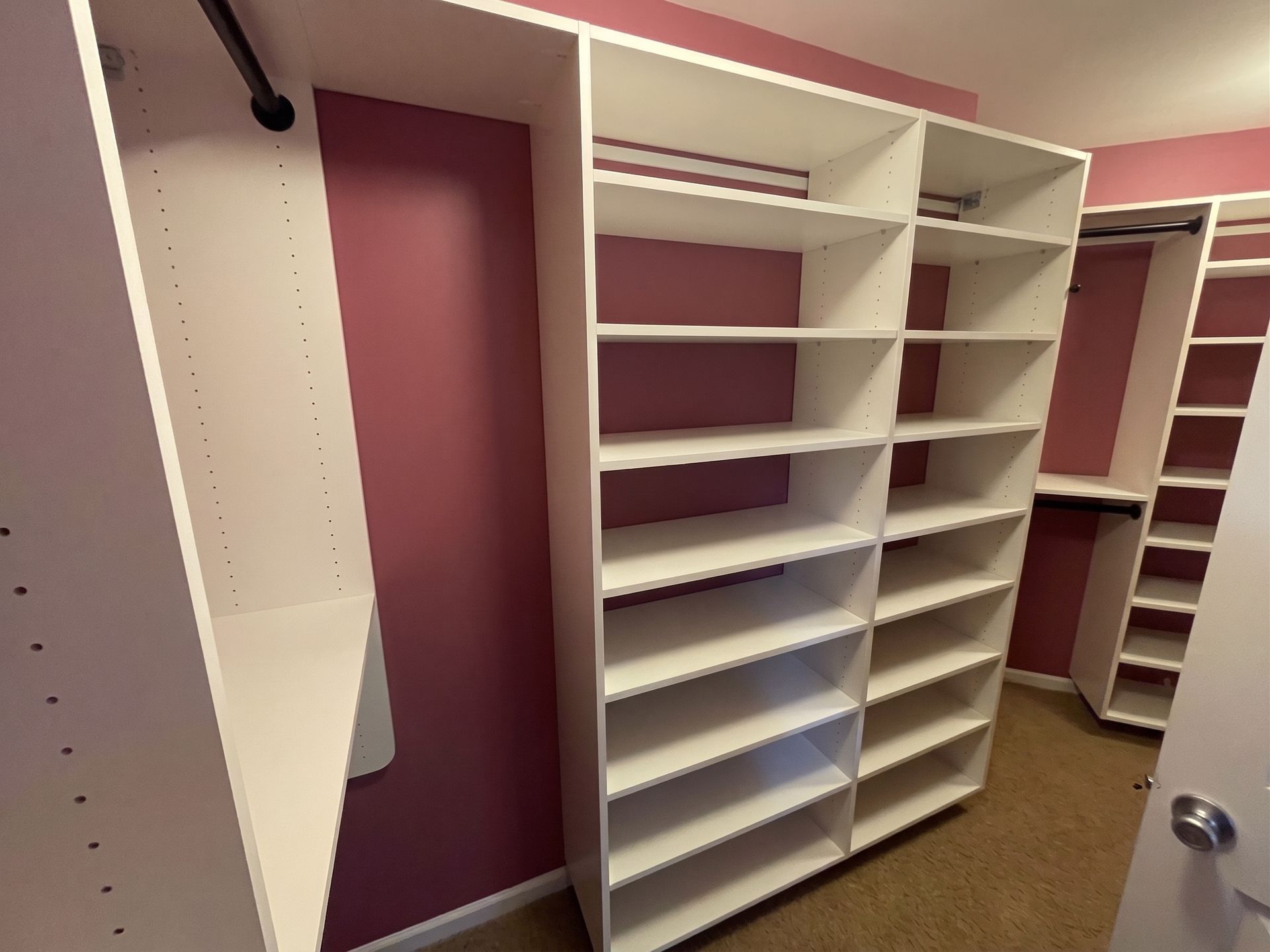 Empty walk-in closet with white shelves and hanging rods against burgundy walls