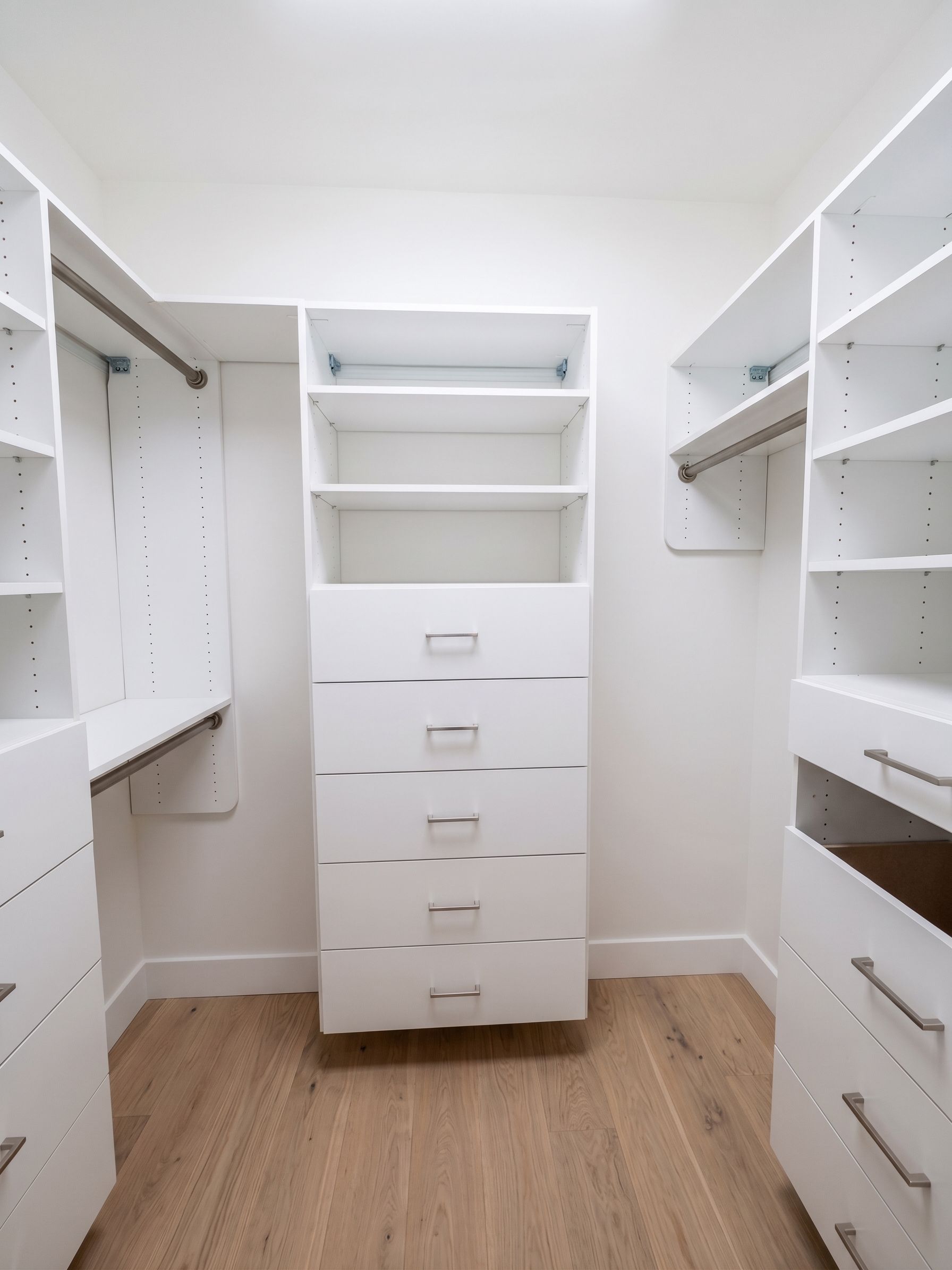 Walk-in closet with white shelving and drawers, light wood floor, and no clothes or items inside.