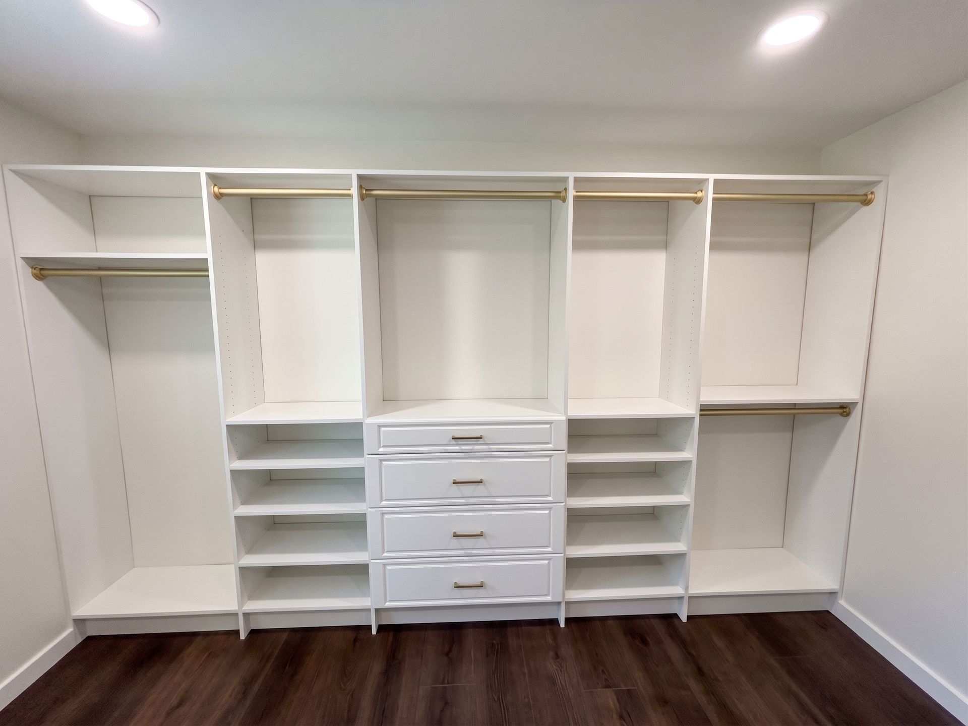 White walk-in closet with shelves, drawers, and hanging rods on a hardwood floor.