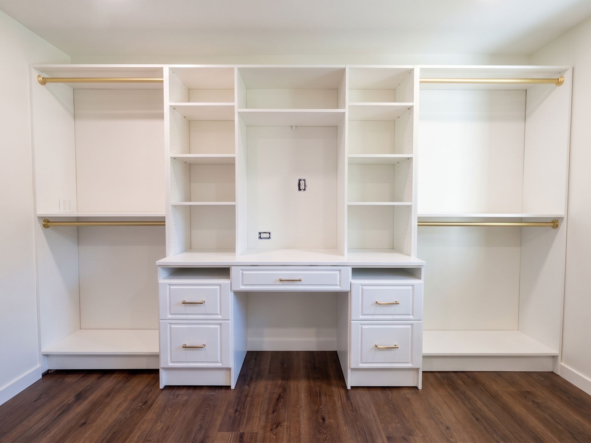 White built-in closet and desk unit with shelves, drawers, and hanging rods in a bright room