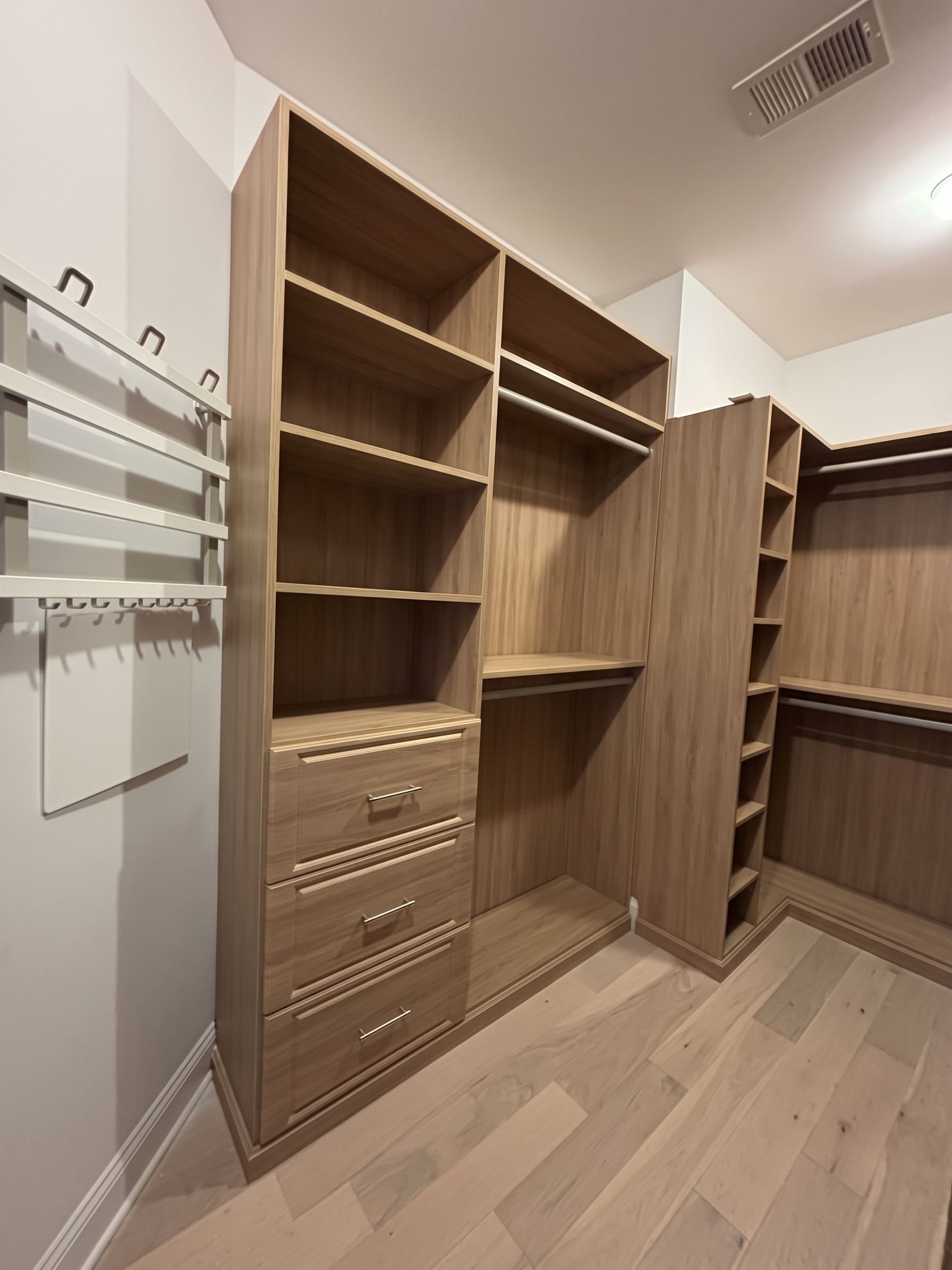 Walk-in closet with wood shelving, drawers, hanging rods, and an open door panel in a bright room