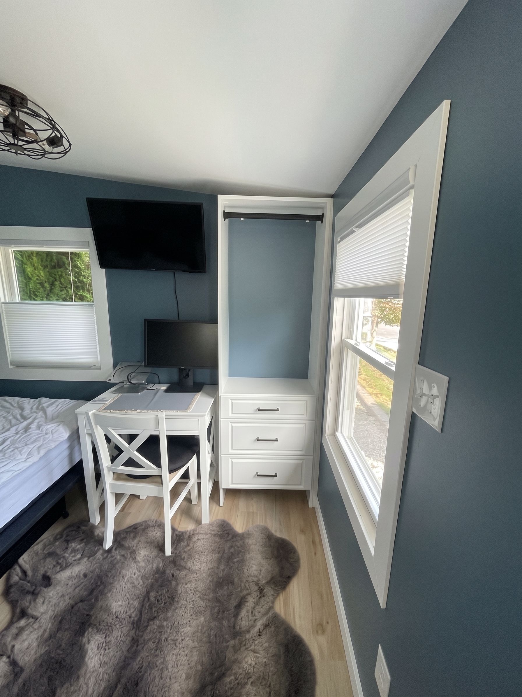 Small gray bedroom with desk nook, white chair, window, and bed along the left wall.
