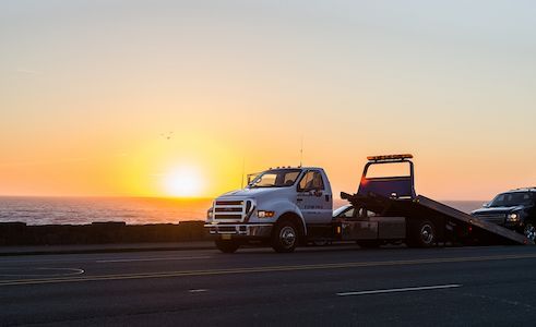 Tilt Tray Truck On The Road Towing Car — Tyre Service in Springsure, QLD