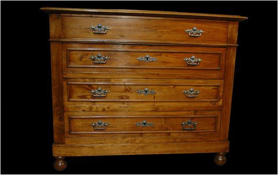 Cassettiera in legno marrone chiaro con quattro cassetti, maniglie e piastre decorative in metallo e piedini arrotondati su sfondo nero.
