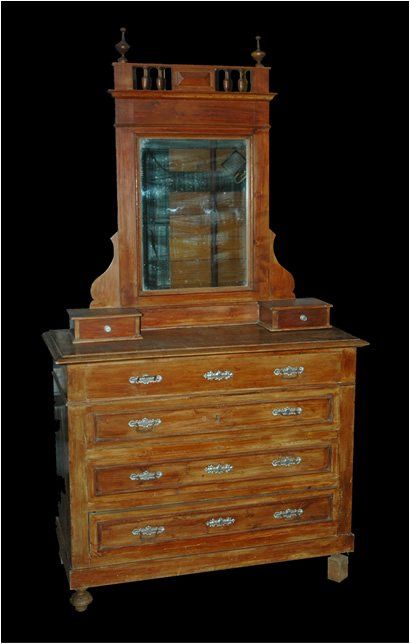 Una cassettiera in legno con specchio, piccoli cassetti laterali e una ringhiera superiore decorativa, posta su uno sfondo nero.