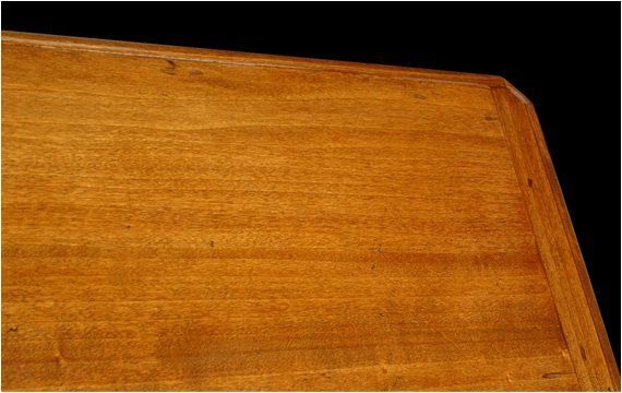 Primo piano di un tavolo in legno liscio color miele con venature visibili, caratterizzato da un bordo smussato su uno sfondo nero.