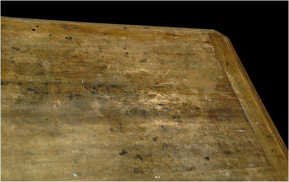 Primo piano dell'angolo di una superficie di legno marrone chiaro usurata, con graffi e macchie scure.