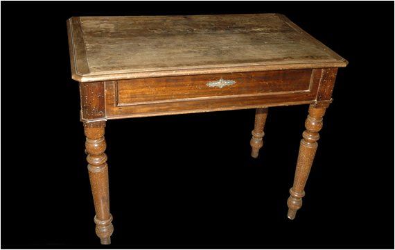 Un tavolino di legno con un solo cassetto e gambe tornite, centrato su uno sfondo nero.