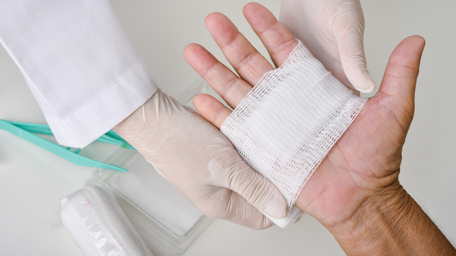 A medical professional in white gloves applying a gauze bandage to a patient's palm.