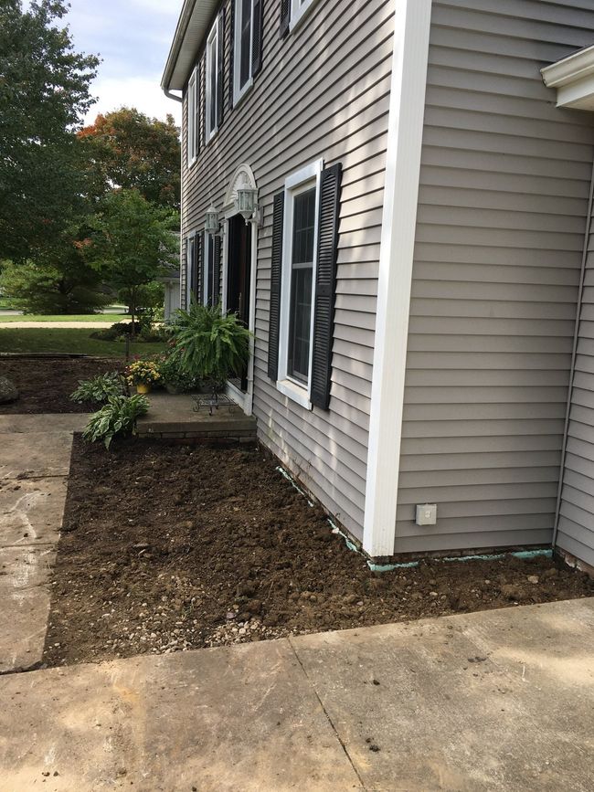 Side of a gray house with black shutters, small mulched planting bed, and concrete walkway