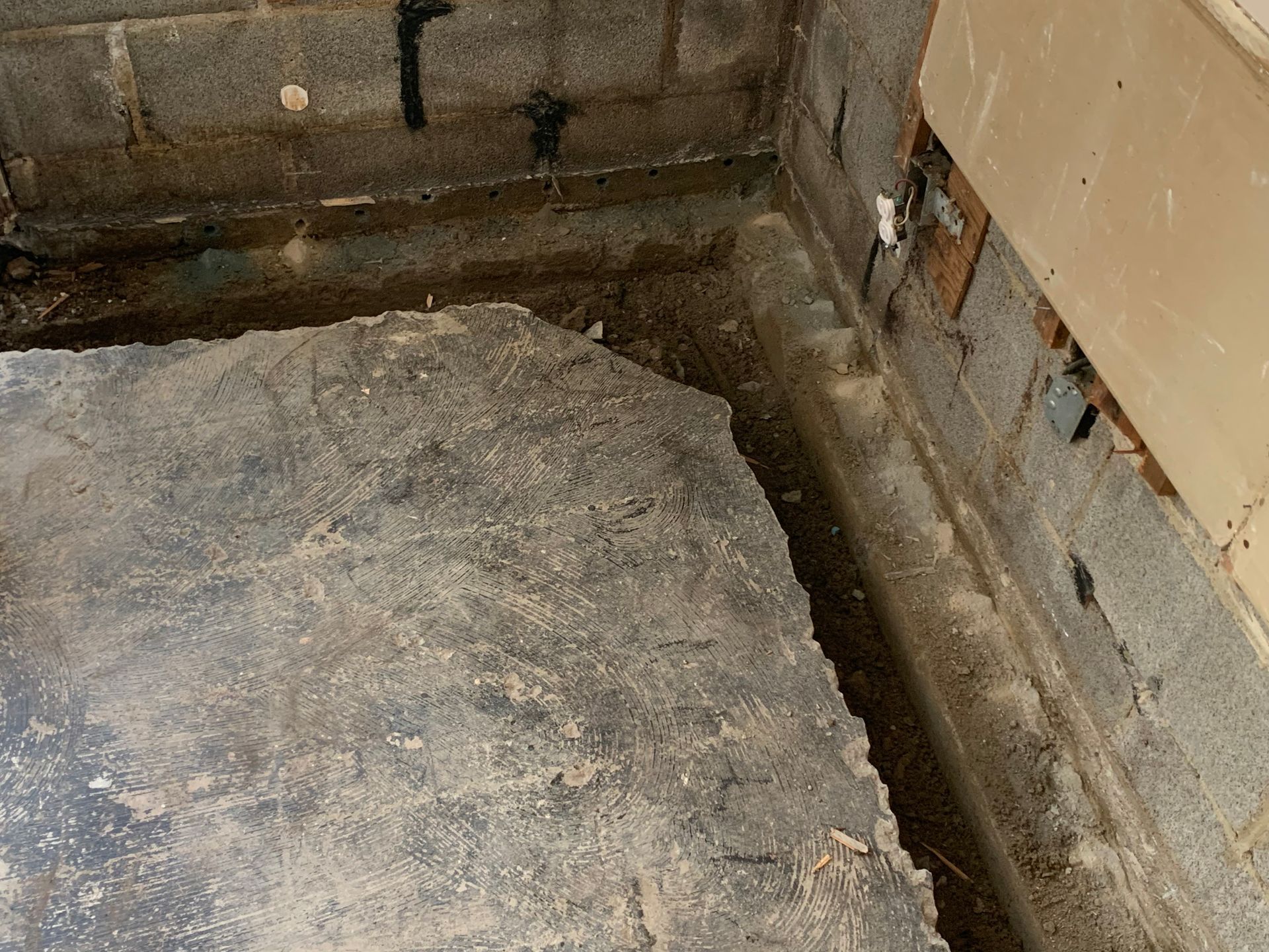 Damaged concrete floor beside a wall with exposed bricks and peeling plaster
