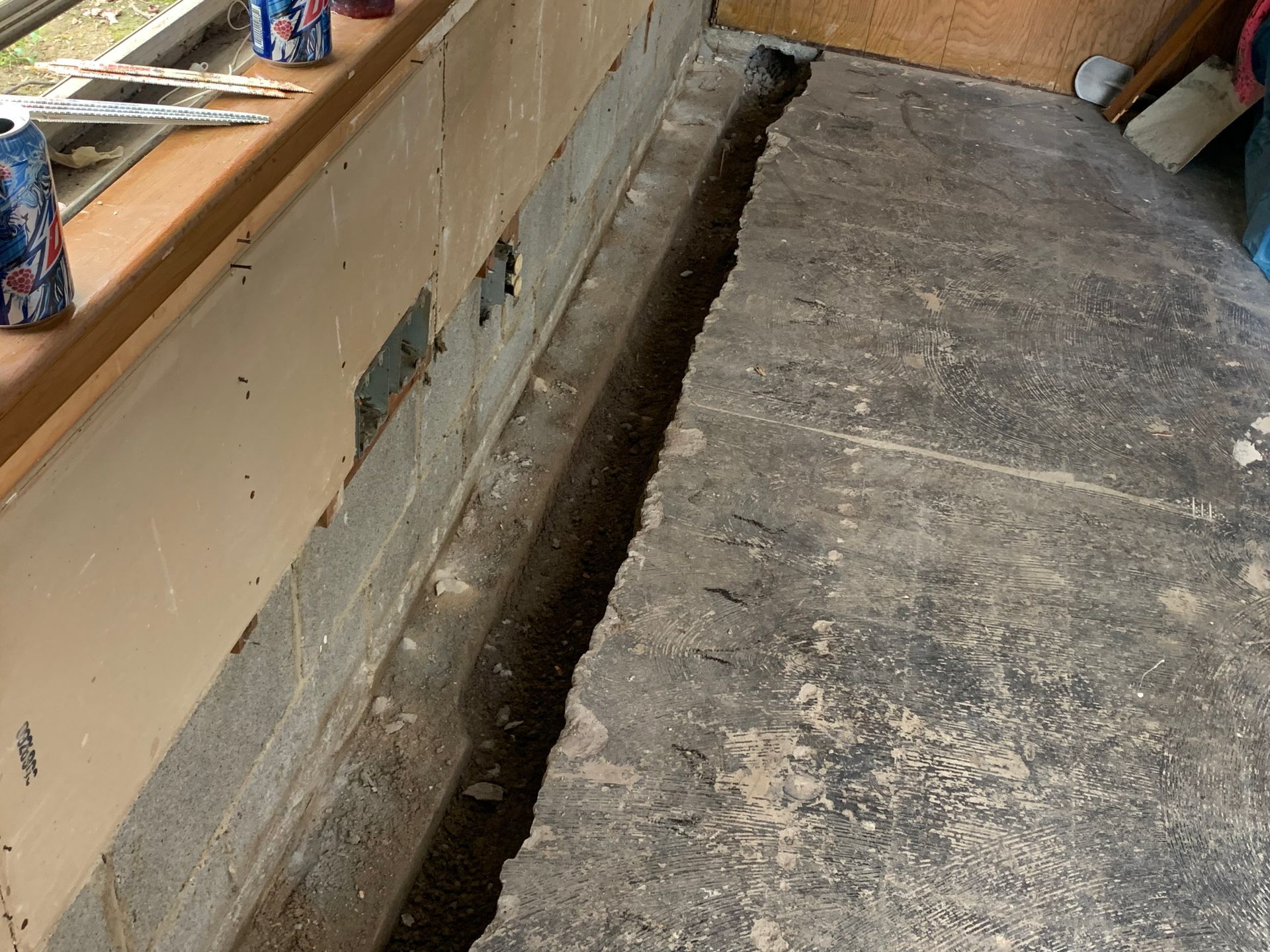 Damaged floor with a long trench gap beside a wall in an unfinished room