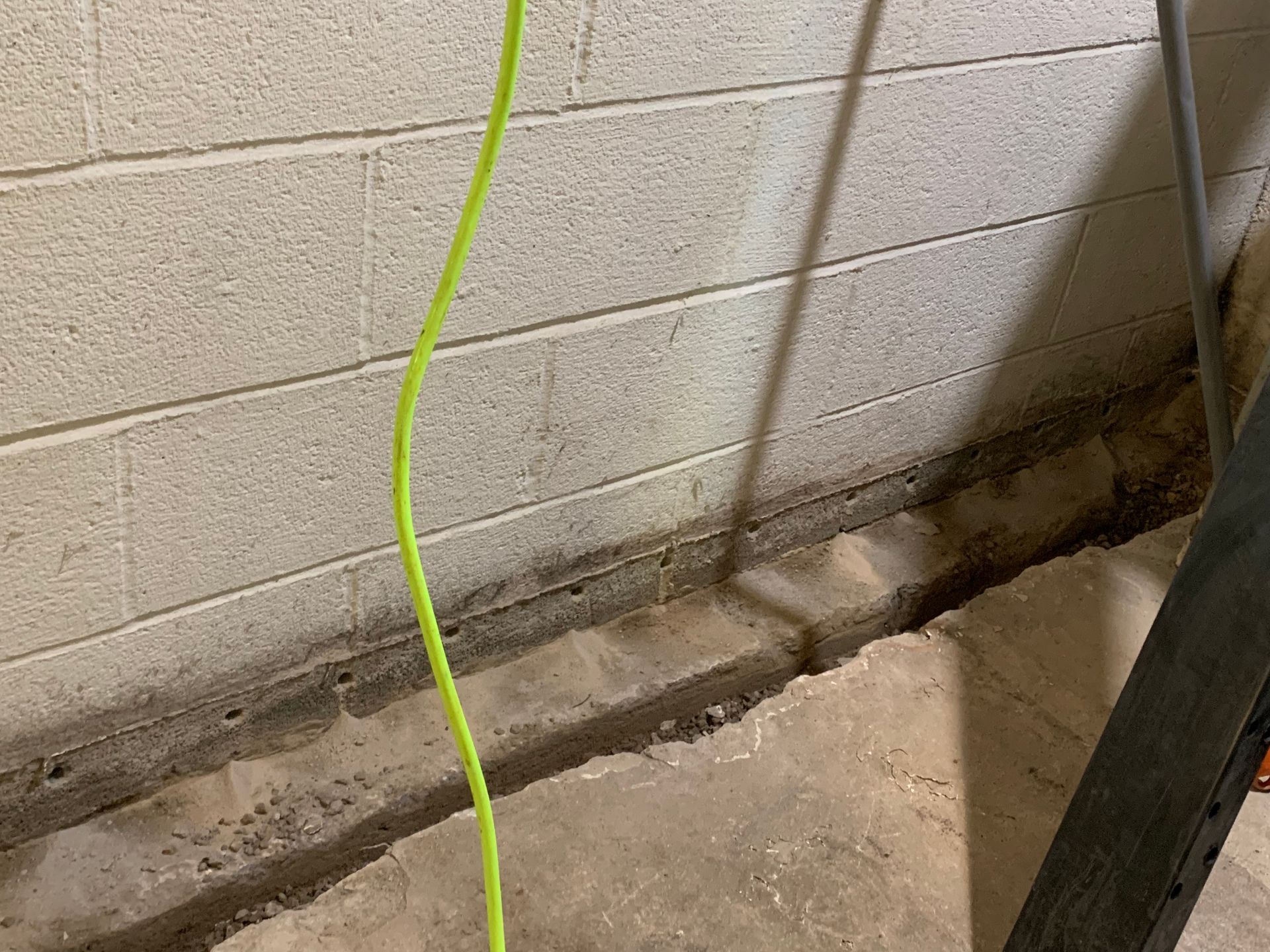 Cracked concrete floor beside cinder block wall with damp stains and a bright green cord hanging down