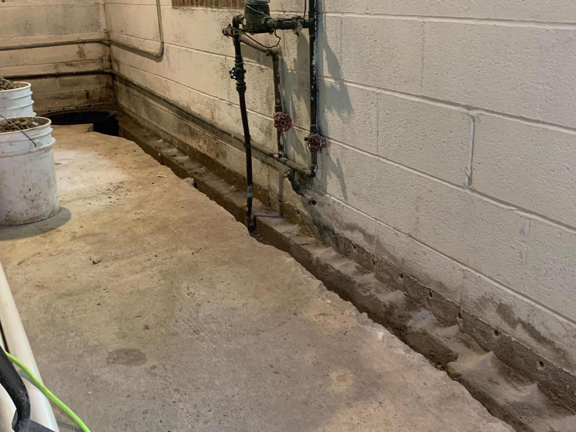 Basement utility area with concrete floor, cinder block wall, and exposed pipes along the wall