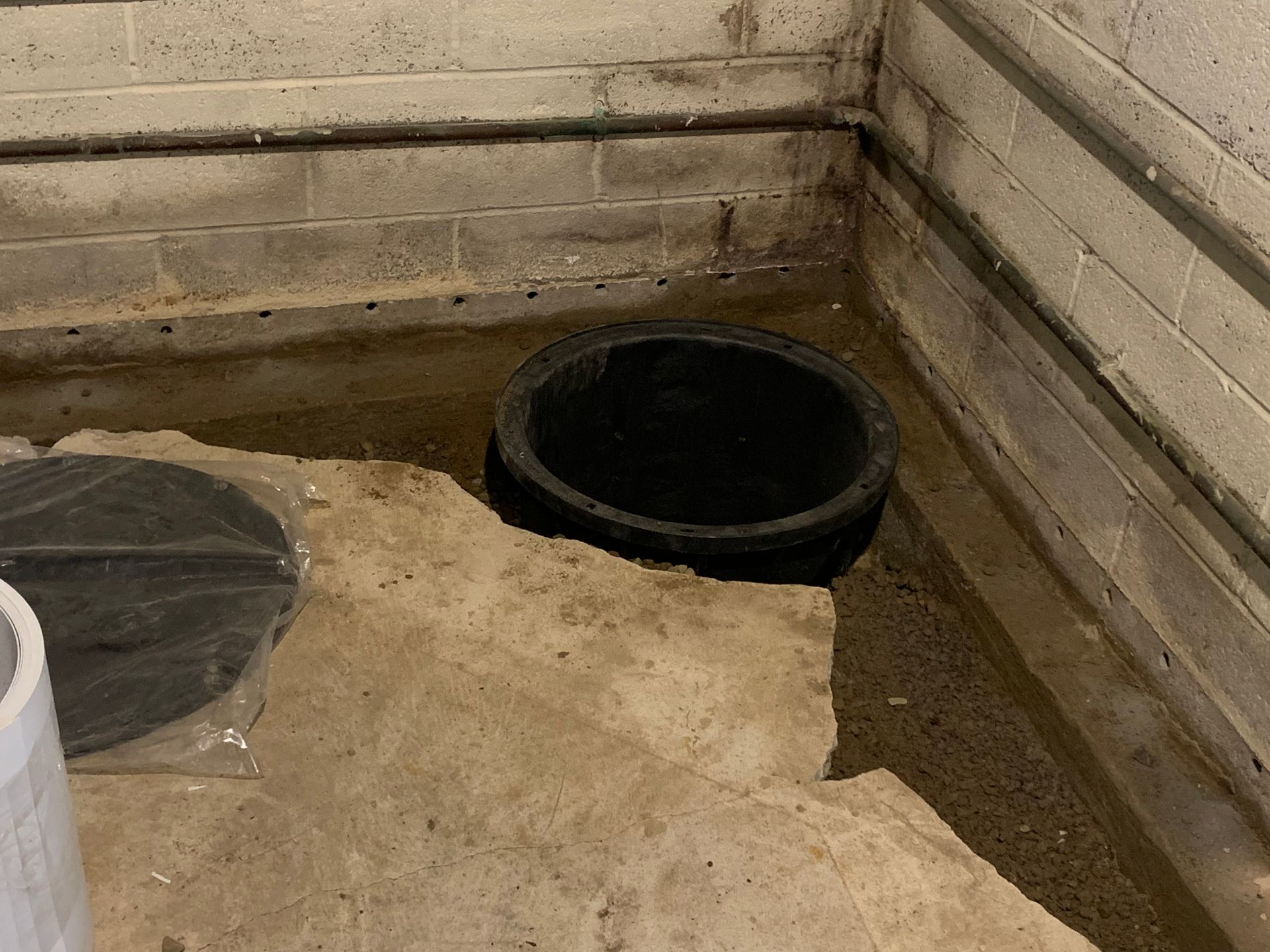 Basement corner with a black floor drain and concrete floor beside wooden walls