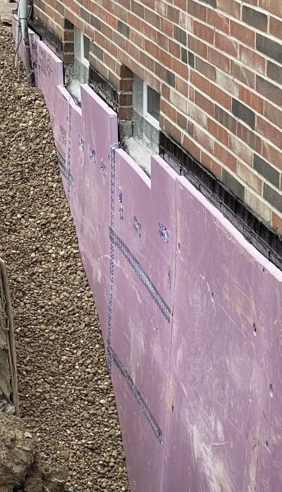 Pink insulation boards lining the base of a brick wall beside gravel ground
