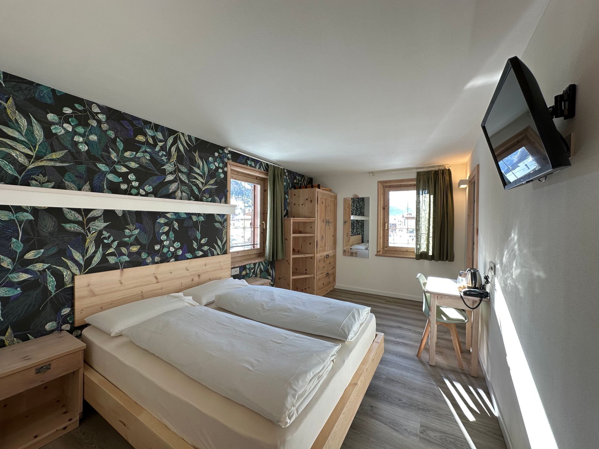 Camera da letto con letto matrimoniale, carta da parati floreale, mobili in legno e TV a parete.
