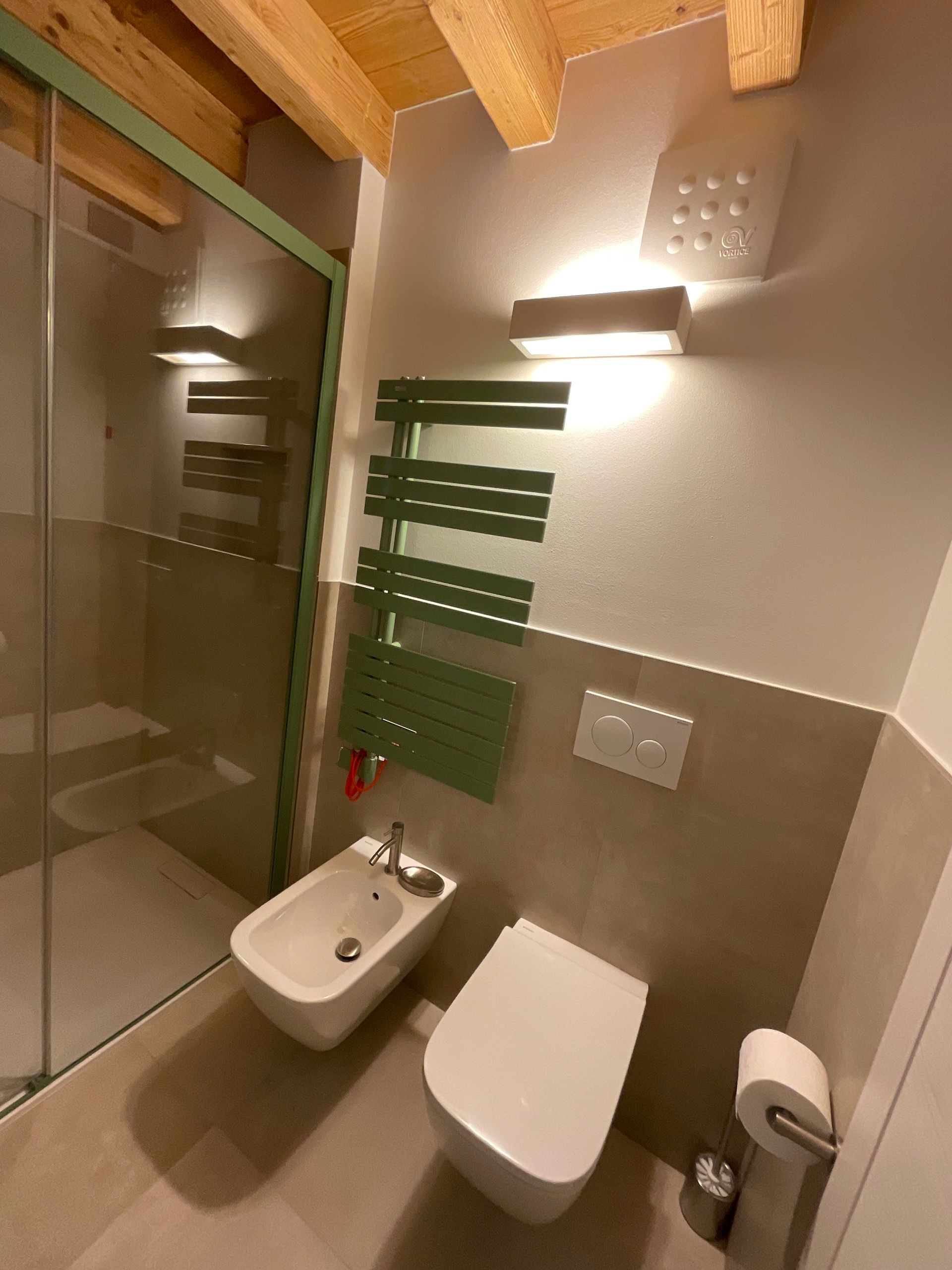 Bagno con dettagli verdi: doccia, scaldasalviette, bidet, WC e applique. Toni beige e bianco.
