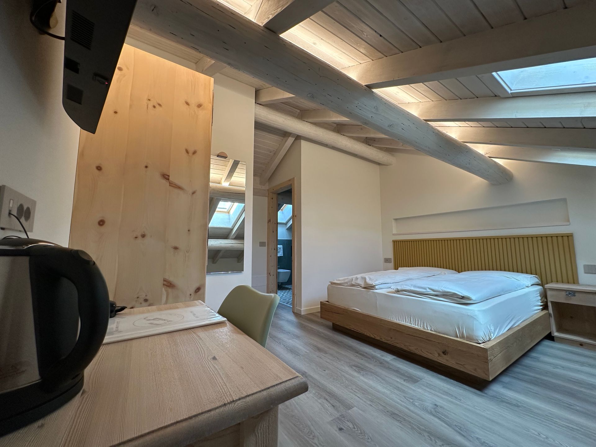 Una camera d'albergo con letto, scrivania, bollitore, travi in ​​legno e lucernario.