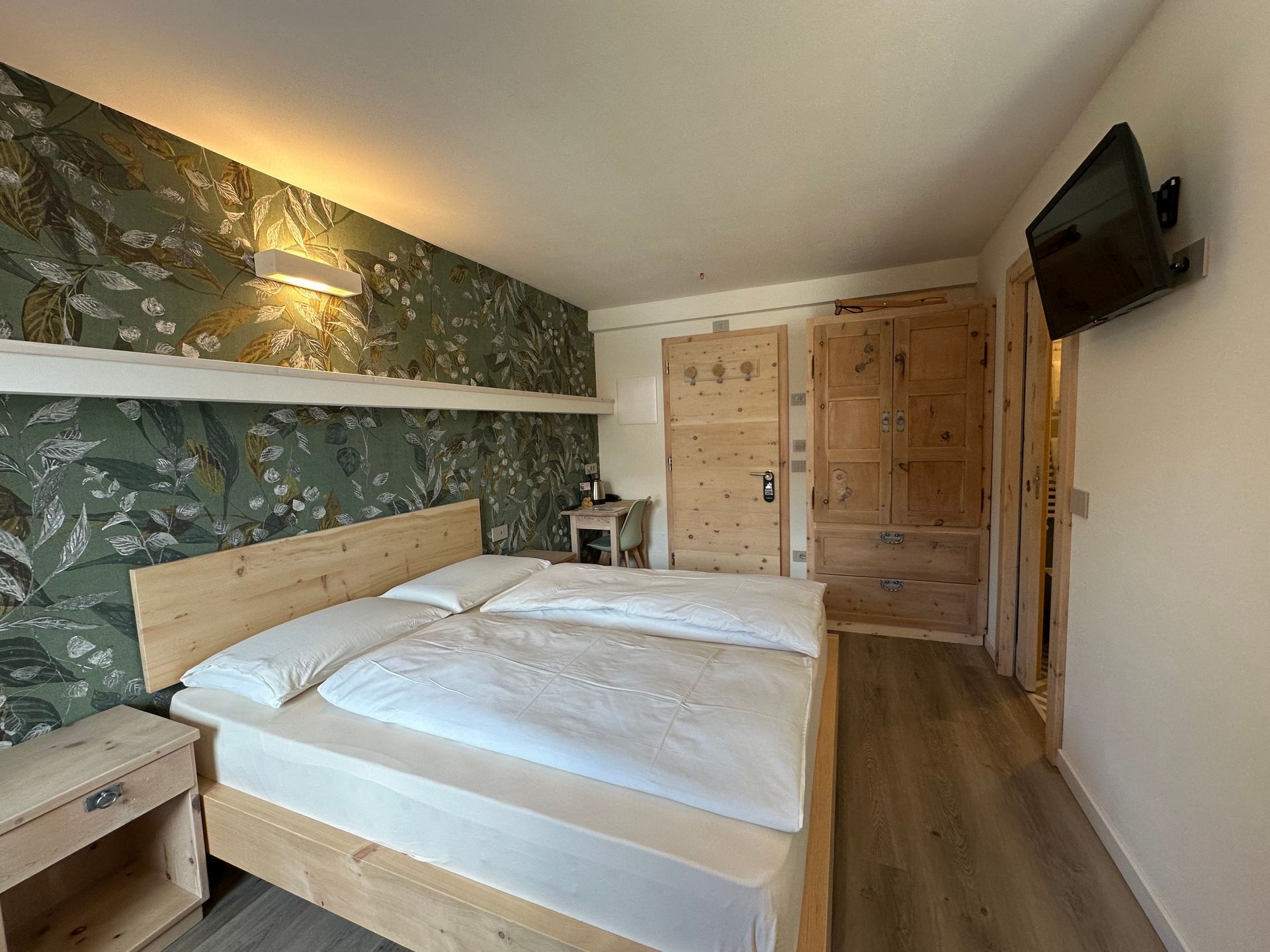 Camera da letto con struttura del letto in legno, carta da parati floreale, porte in legno e TV a parete.
