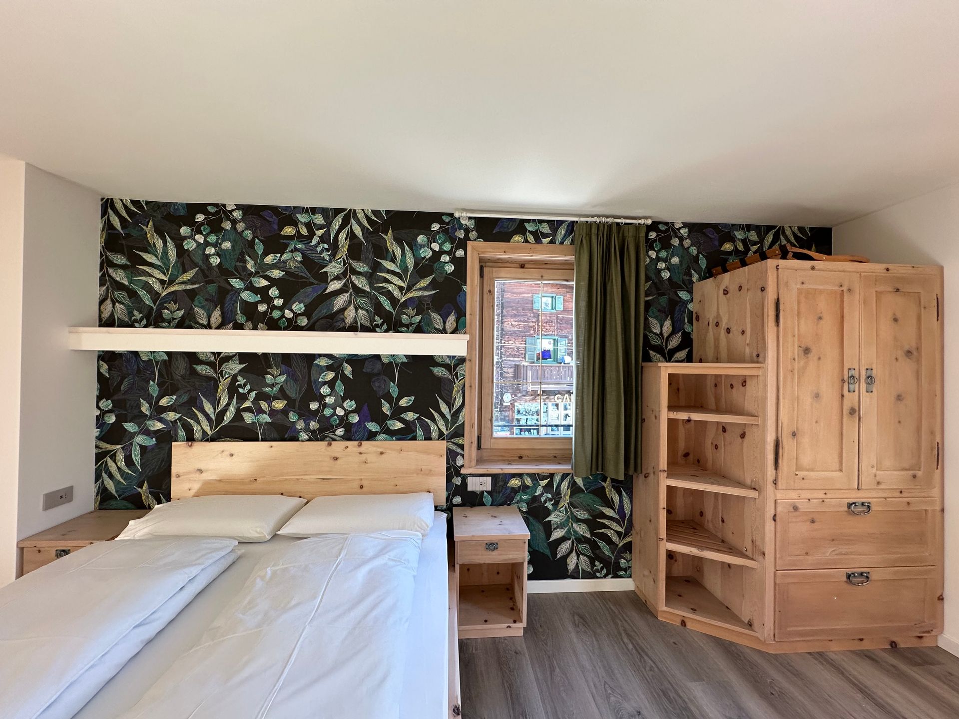 Camera da letto con letto matrimoniale, carta da parati floreale, mobili in legno e finestra con vista sull'esterno.