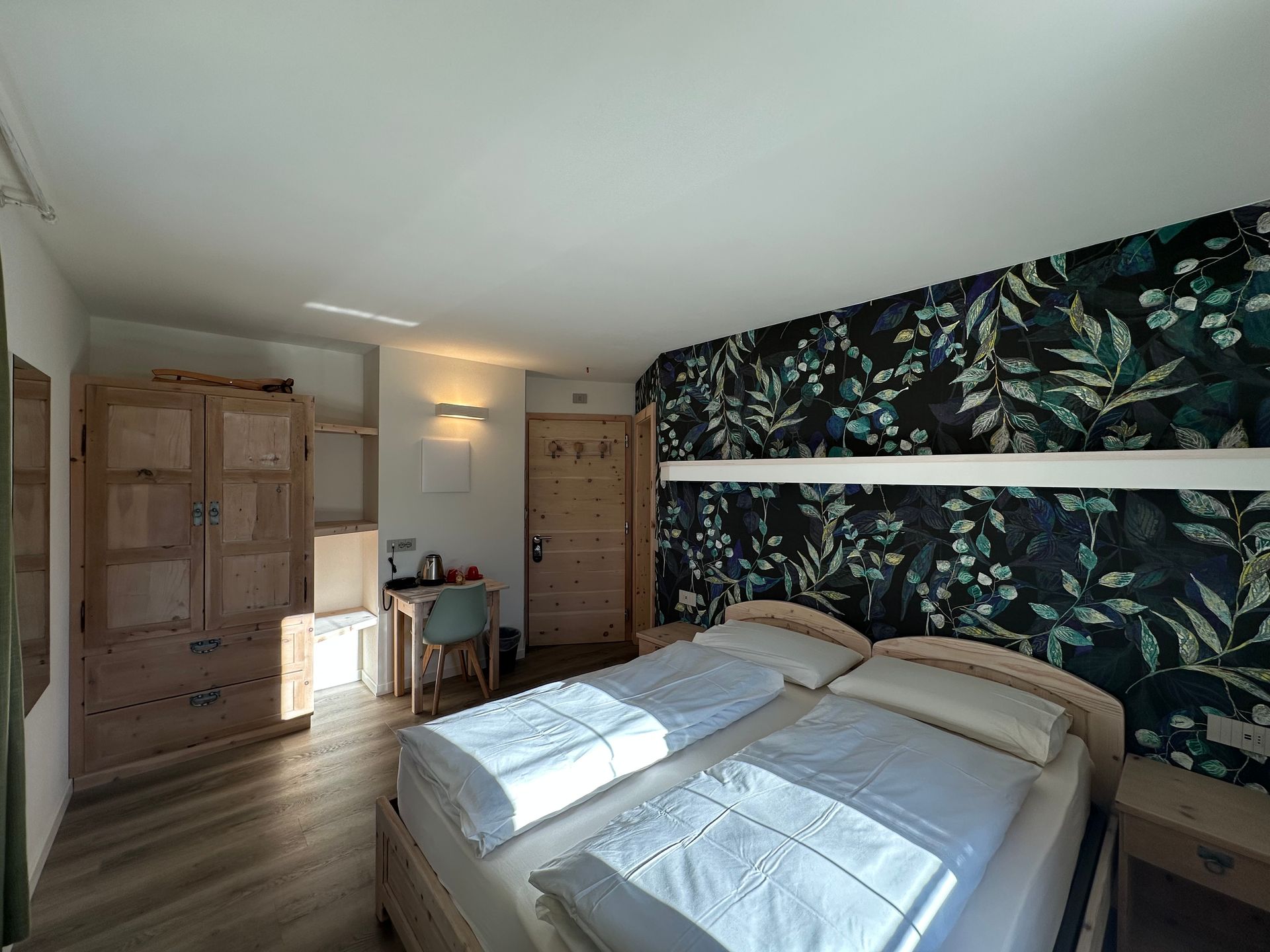 Camera da letto con letto, parete decorativa con carta da parati floreale, armadio in legno, scrivania e porta.