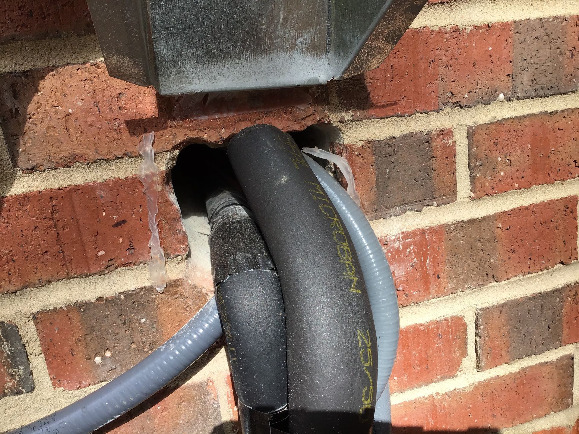 A brick wall with a hose attached to it that can be used as an entry point for wildlife or critters.