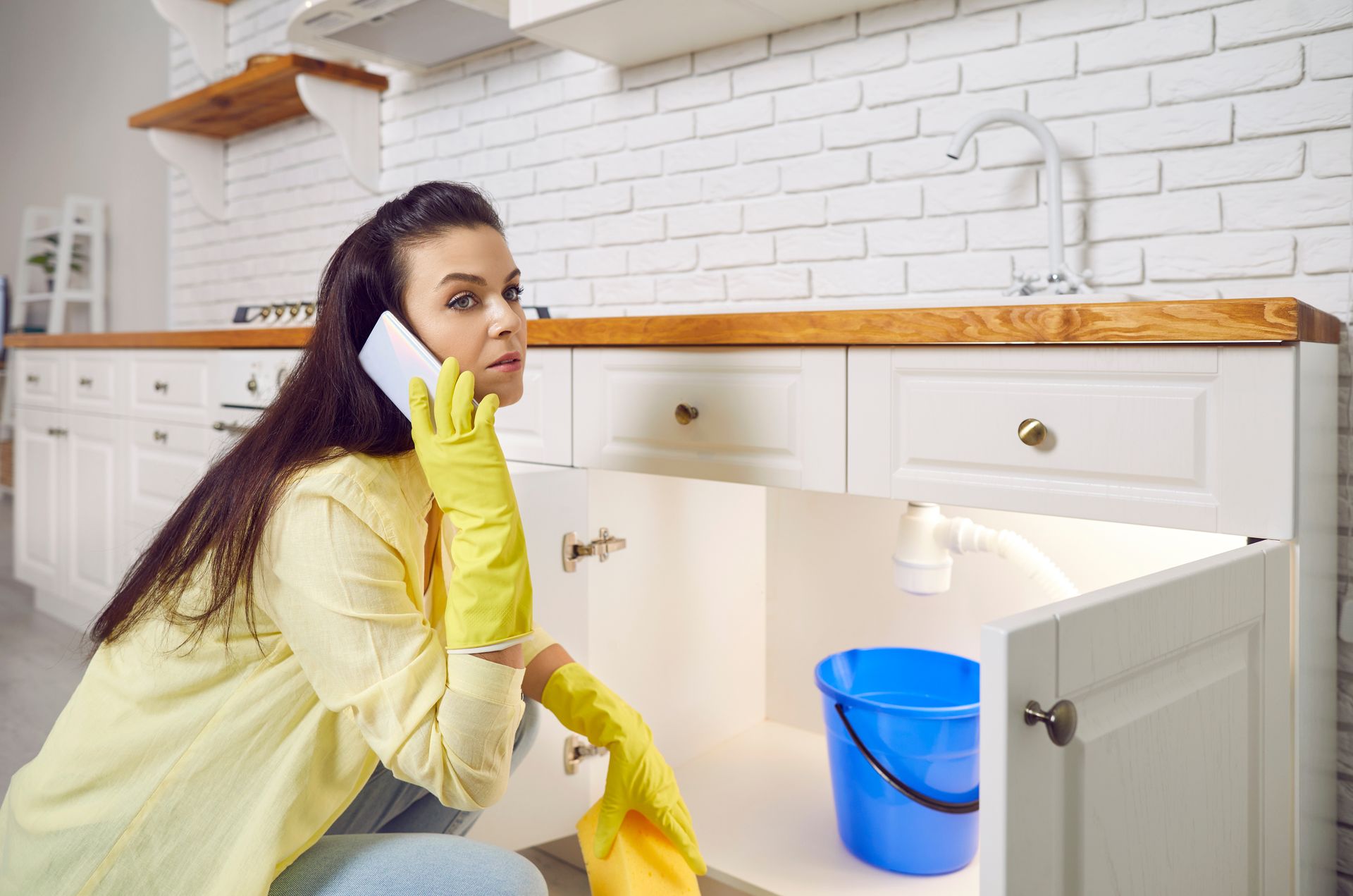 A woman crouching in front of an open kitchen cabinet with a blue bucket inside. A woman crouching in front of an open kitchen cabinet with a blue bucket inside.