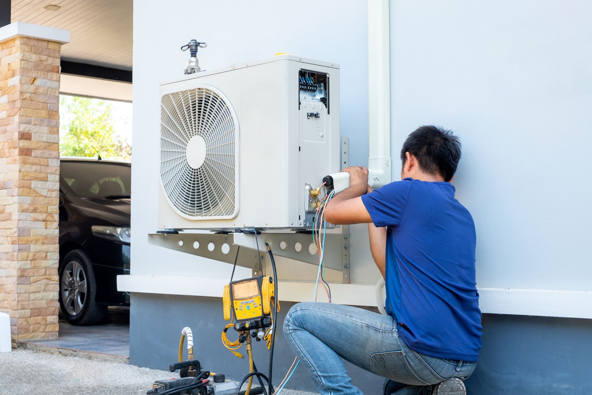 Technician connecting lines and testing an outdoor air conditioning unit during installation.