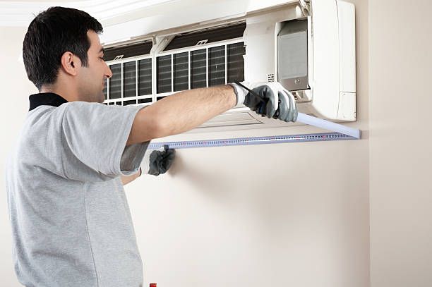 A technician wearing gloves is measuring a wall for an air conditioning install.