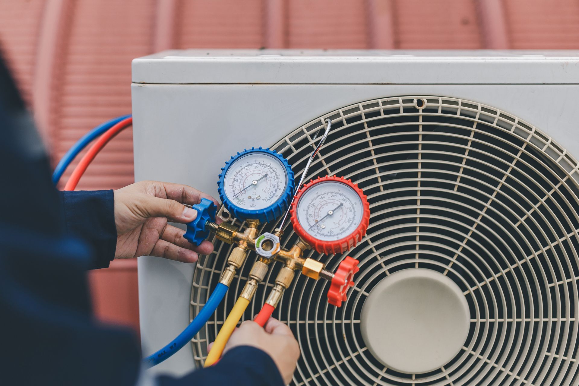 An HVAC service technician uses gauges to check refrigerant and add refrigerant for HVAC repair.