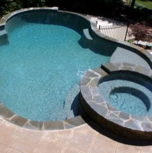 Pool with attached jacuzzi, both filled with water, surrounded by stone edging and a patio.