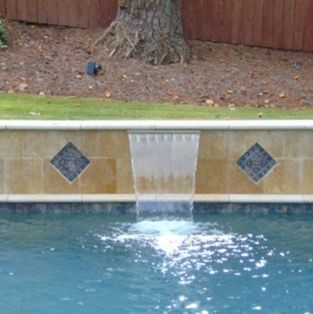 Pool with waterfall feature and decorative tile on a stone wall.