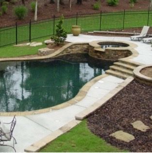 Pool with a raised spa, stone steps, and surrounding patio, edged by a black fence.