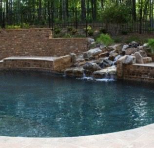 Swimming pool with waterfall feature, stone walls, and surrounding greenery.