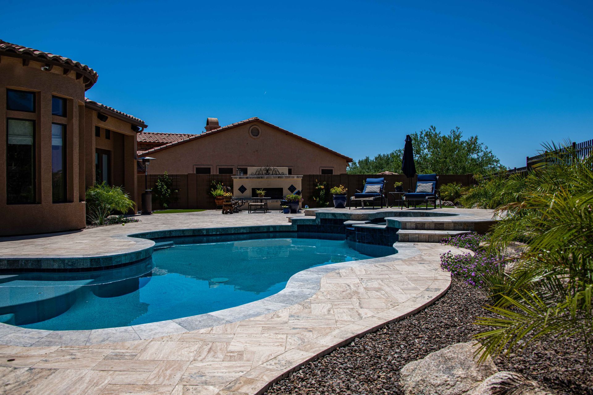 Swimming pool and patio with a house in the background on a sunny day.