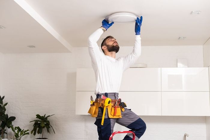 A man is standing on a ladder installing a light fixture on the ceiling.