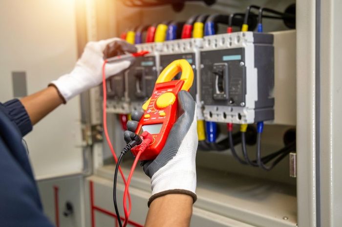 An electrician is using a clamp meter to test an electrical box.