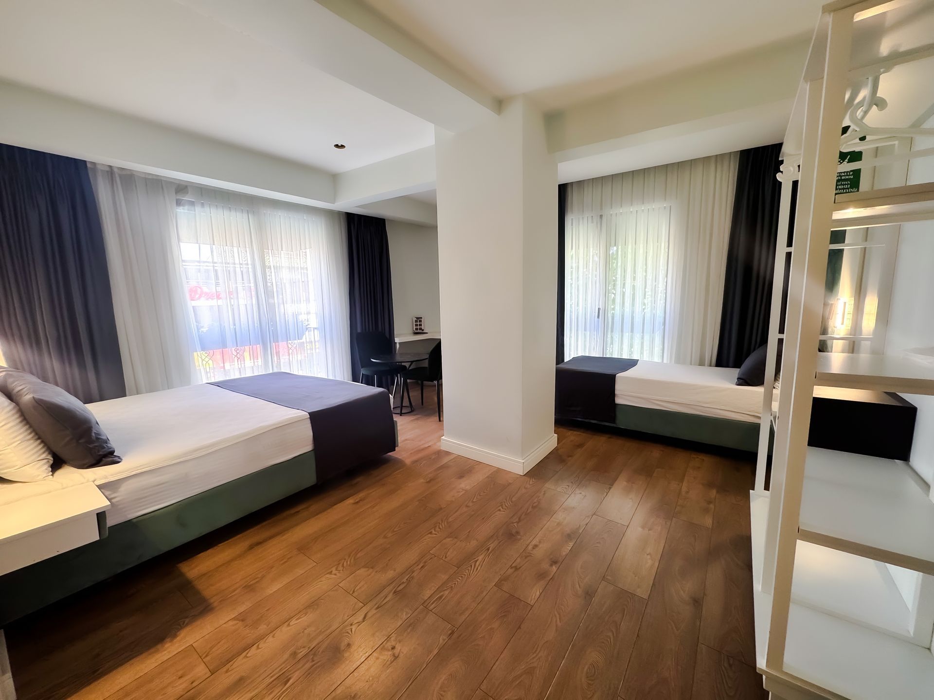 Bright modern bedroom with two beds, large windows, and wood flooring