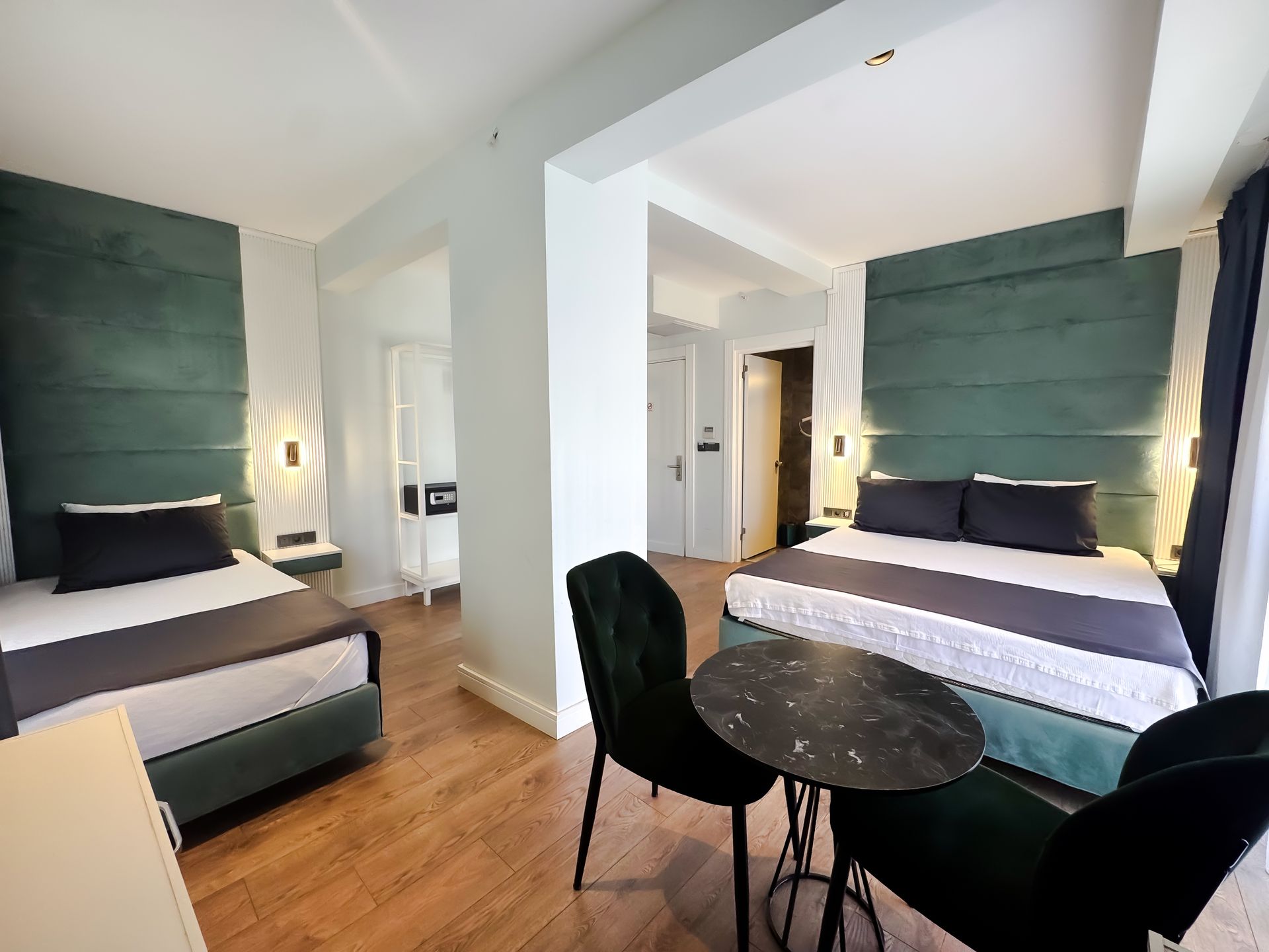 Modern hotel room with two beds, teal headboards, and a small round table with two black chairs.