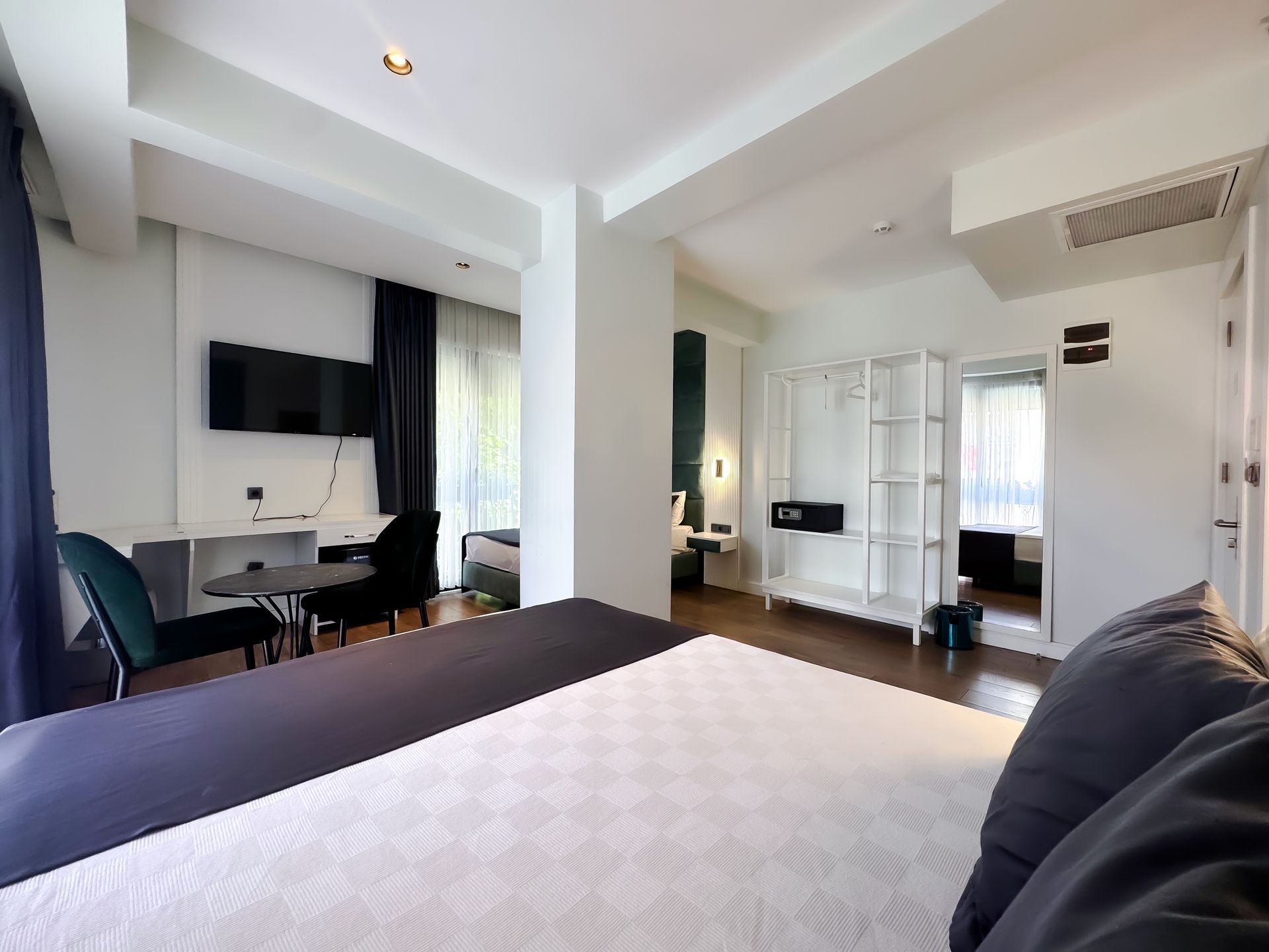Bright bedroom with a bed, desk, wall TV, and sliding doors leading to a balcony